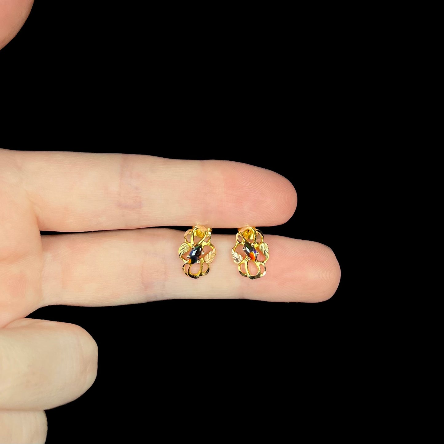 Fingers holding marquise cut synthetic black opal earrings with Black Hills gold grape leaf motif