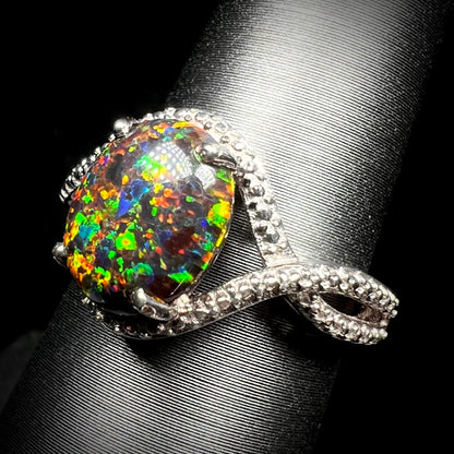 A lab-created black opal solitaire ring with green color play in sterling silver, shown from an angle on a ring display.