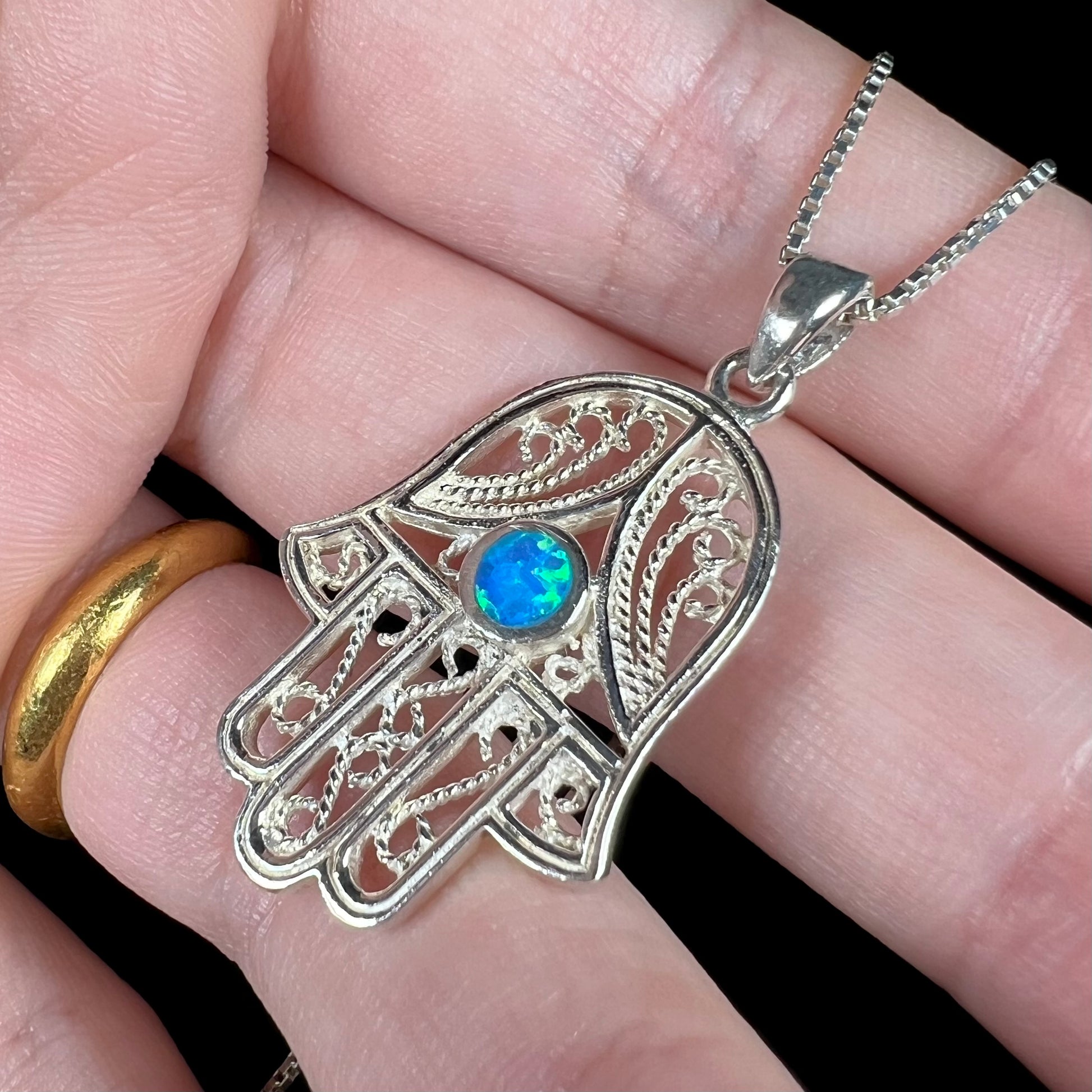 A sterling silver and filigree-accented hamsa hand necklace set with a round lab-created opal.