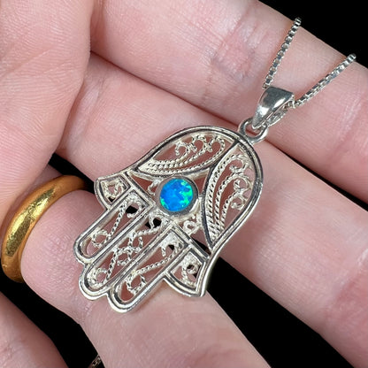 A sterling silver and filigree-accented hamsa hand necklace set with a round lab-created opal.