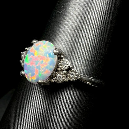 Angled shoulder view of synthetic opal ring focusing on illusion set natural diamond accents, shown on ring display.  The opal has a bright red flash of color.