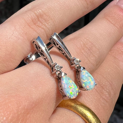 A pair of sterling silver filigree dangle earrings mounted with pear shaped lab created opals and diamond accents.