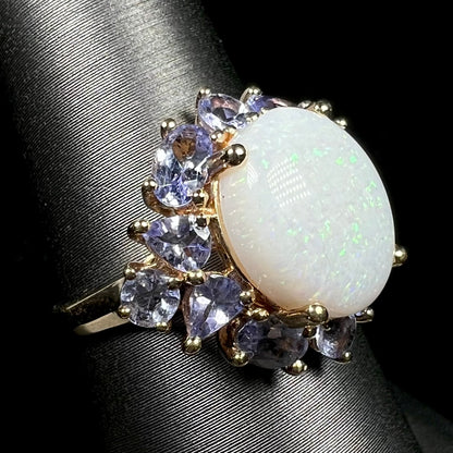 A 14k yellow gold Australian white opal ring with tanzanite accents, shown on ring display from angled view