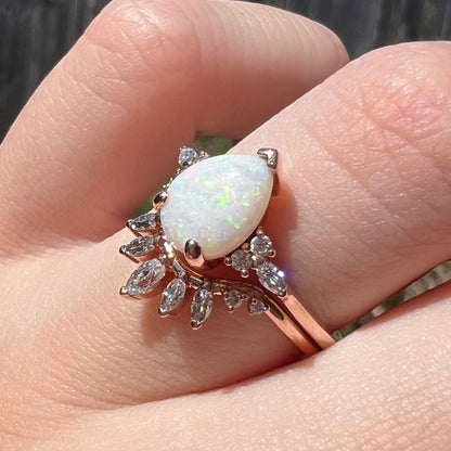 Two-piece teardrop-shaped opal and moissanite wedding ring set, worn on finger in sunlight