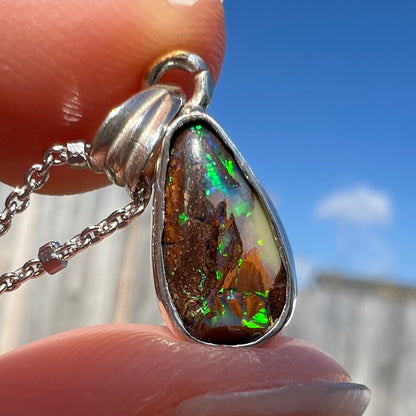 A pear shaped boulder opal necklace in sterling silver.  The opal has bright green and blue flashes.