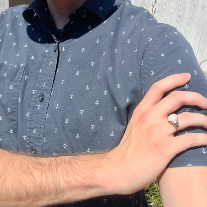 Close-up of person resting hand on opposing shoulder in sunlight wearing a white gold opal ring with textured shoulder designs