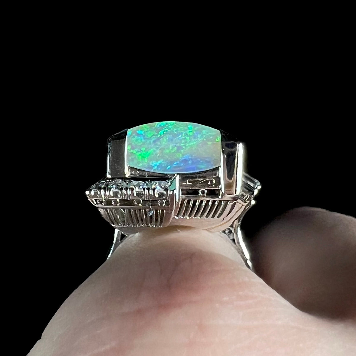 Gallery view of a vintage platinum cocktail ring prong-set with a thickly-cut Australian opal slab that shines with green and blue play-of-color under LED light, worn on hand.