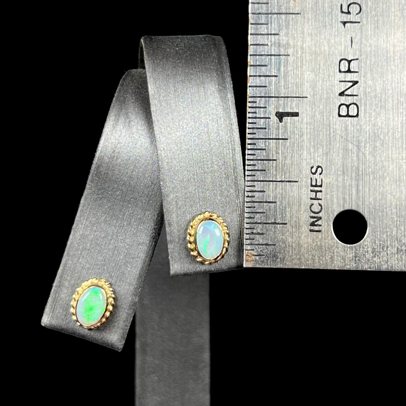 Pair of gold opal stud earrings measuring one-third of an inch on earring display next to ruler.