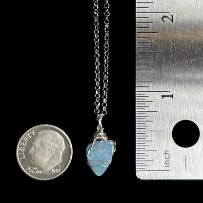 A 0.75 inch long wire wrapped sterling silver opal doublet pendant shown on a chain next to a US dime coin and ruler for scale.