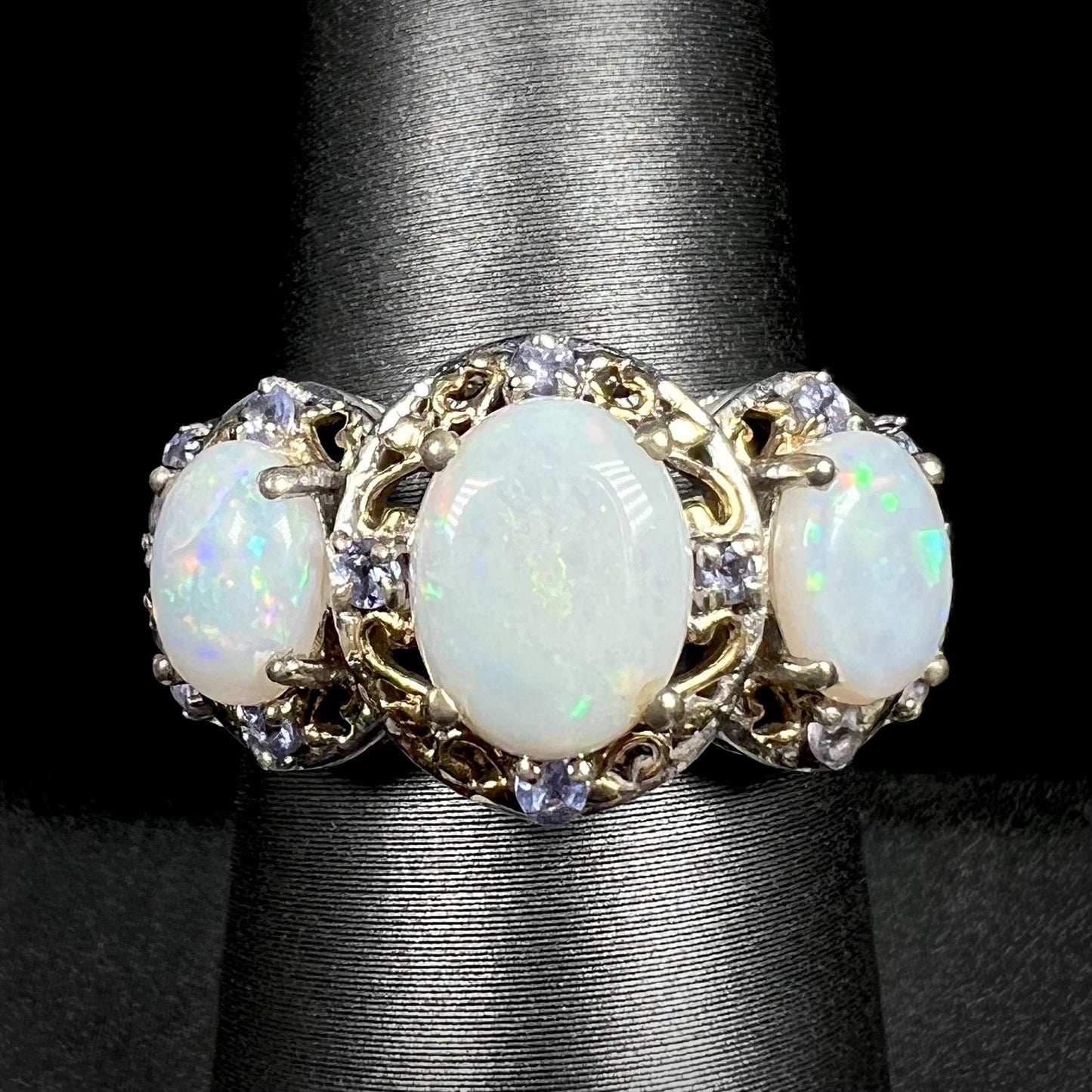 Close-up macro view of a three-stone Australian white opal and tanzanite-accented ring in two-tone sterling silver, shown on a ring display.