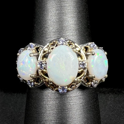 Close-up macro view of a three-stone Australian white opal and tanzanite-accented ring in two-tone sterling silver, shown on a ring display.