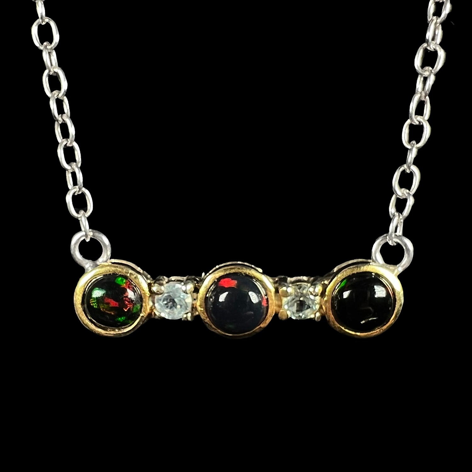 A three-stone black Ethiopian opal and white topaz necklace in two-tone sterling silver, shown close-up.