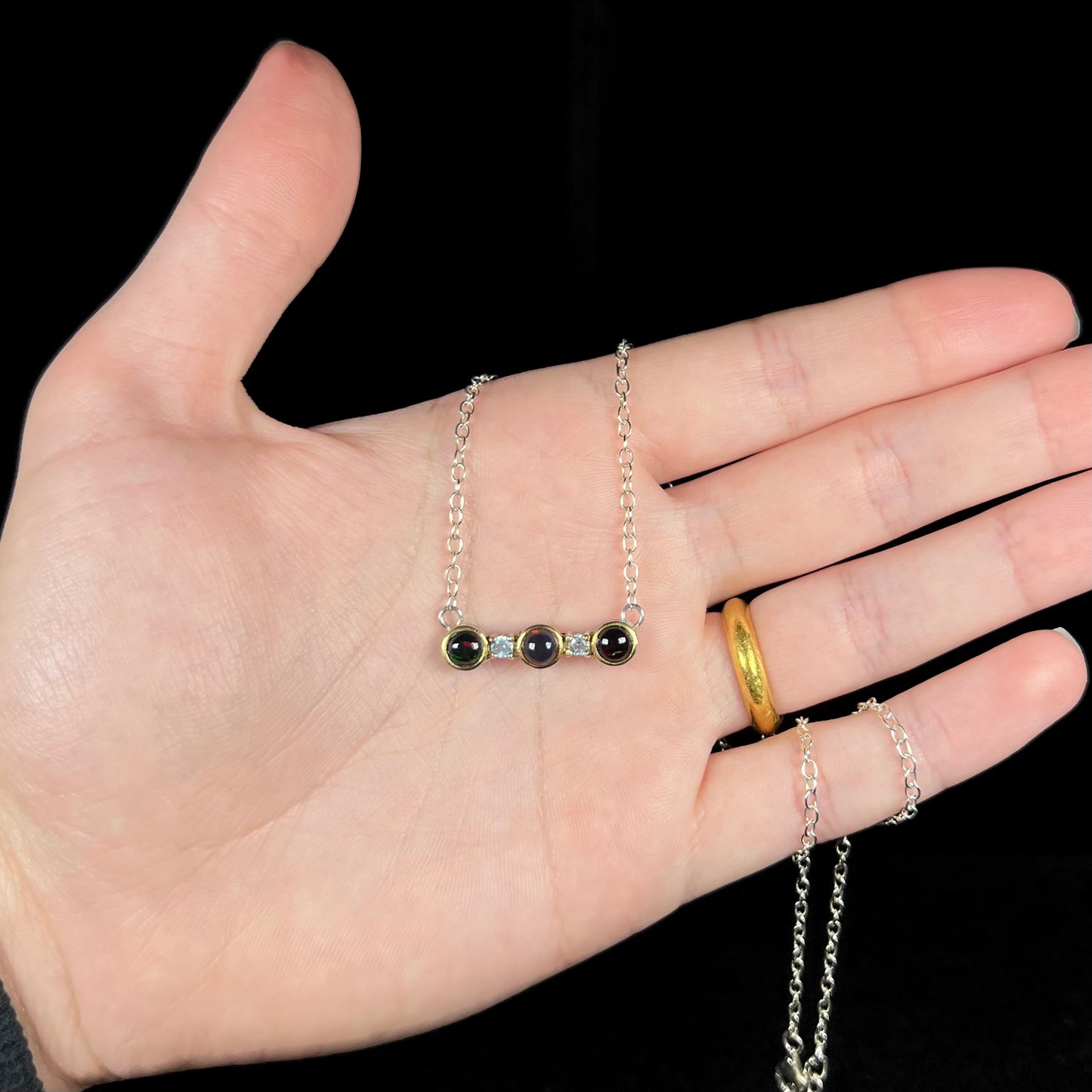 A three-stone black Ethiopian opal and white topaz necklace in two-tone sterling silver shown in a hand.