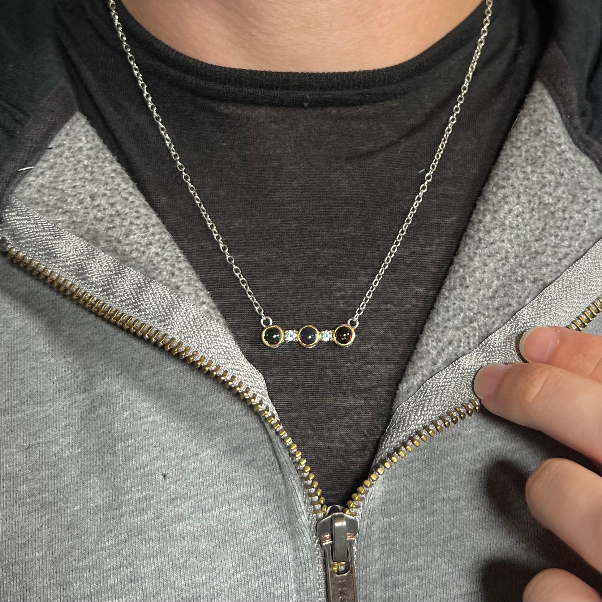A three-stone black Ethiopian opal and white topaz necklace in two-tone sterling silver worn around a neck.