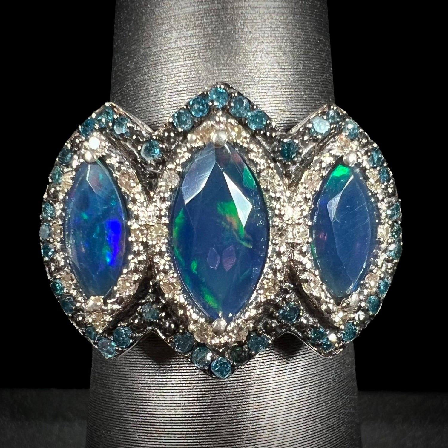 A three-stone marquise opal and blue diamond ring in silver, shown straight-on against a black background.