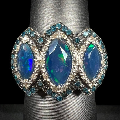 A three-stone marquise opal and blue diamond ring in silver, shown straight-on against a black background.