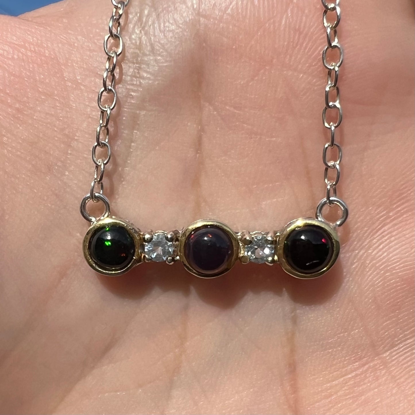 A three-stone black Ethiopian opal and white topaz necklace in two-tone sterling silver.