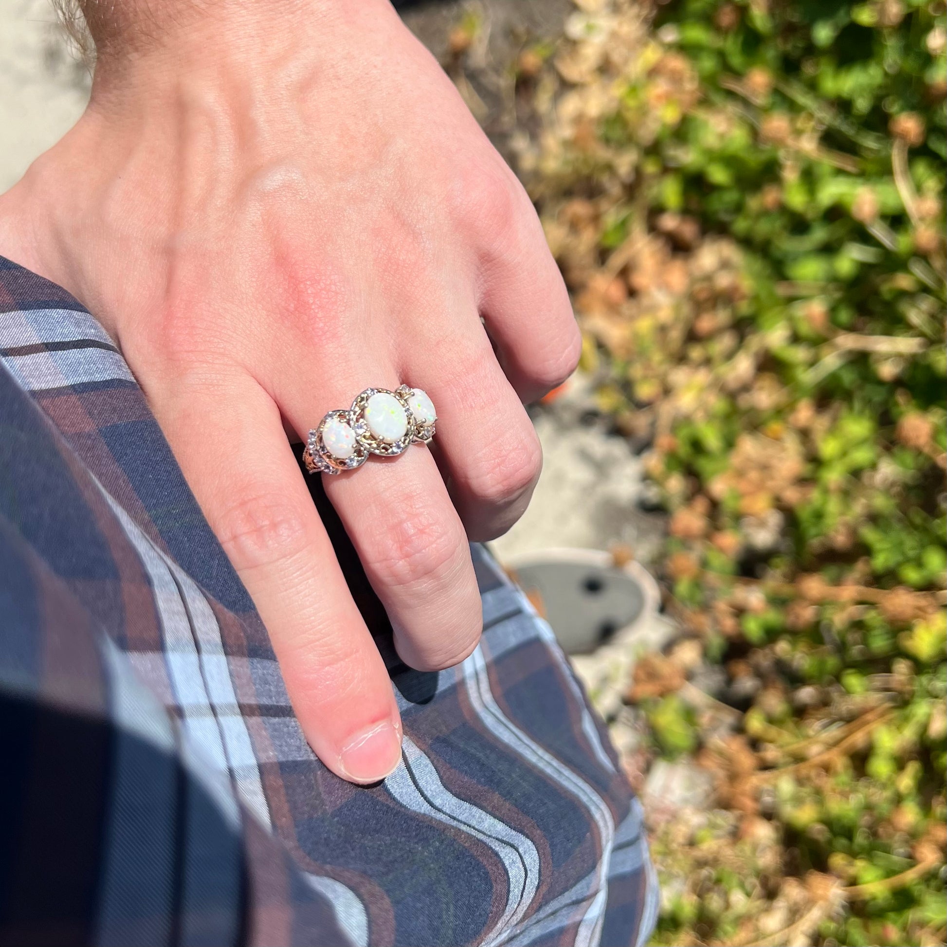 Hand resting on person's hip in sunlight while wearing a three-stone Australian opal and tanzanite ring made from sterling silver.
