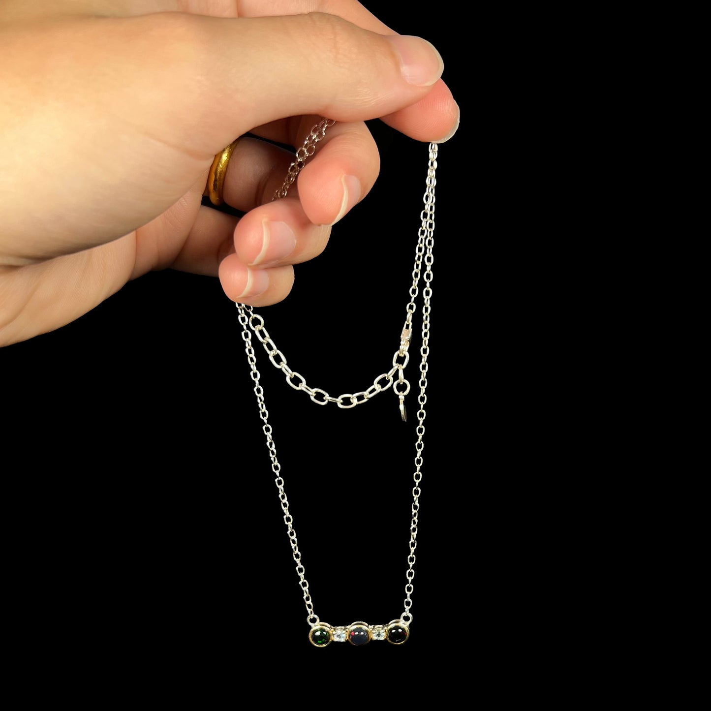A three-stone black Ethiopian opal and white topaz necklace in two-tone sterling silver, dangled by its chain.