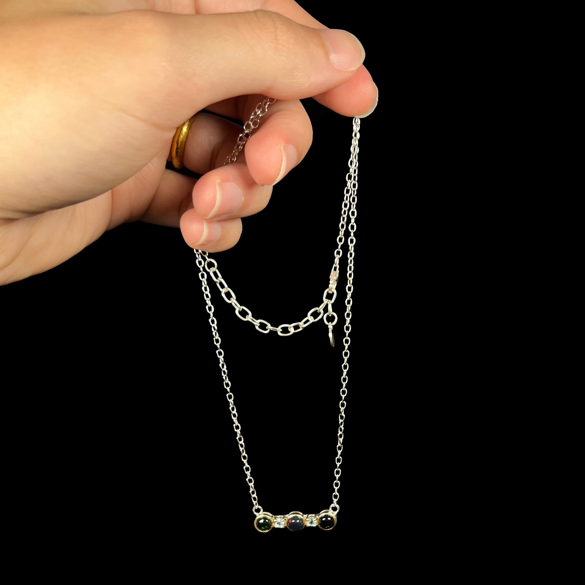 A three-stone black Ethiopian opal and white topaz necklace in two-tone sterling silver, dangled by its chain.
