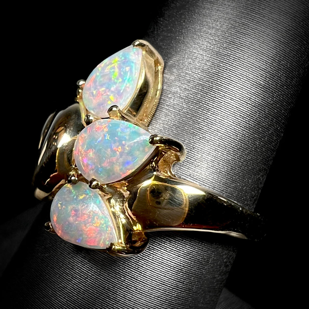 Angled macro view of a three-stone pear shaped Australian crystal opal ring in 14k gold.  The opals glow with pink play of color.