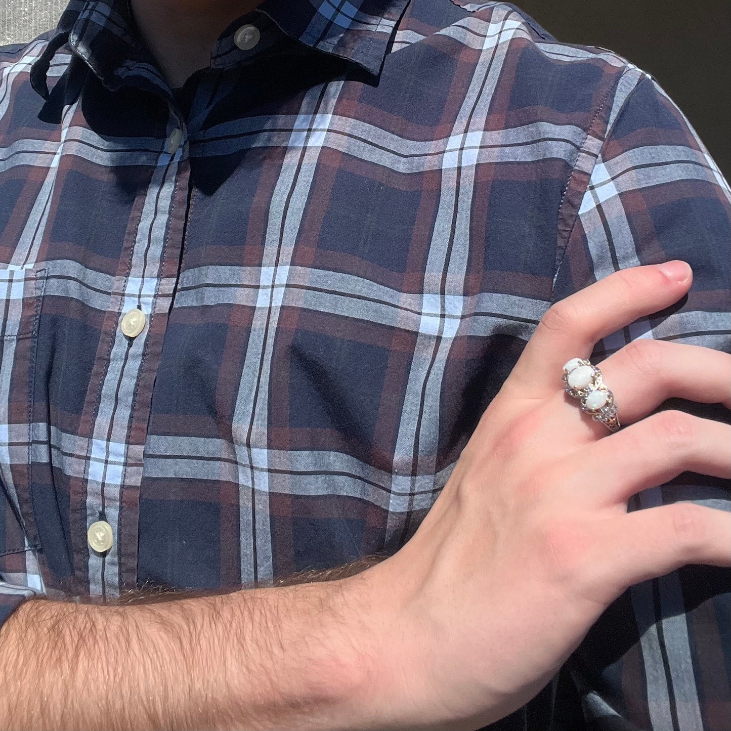 Close-up of person resting hand on opposing shoulder in sunlight while wearing a women's sterling silver three-stone Australian opal ring.