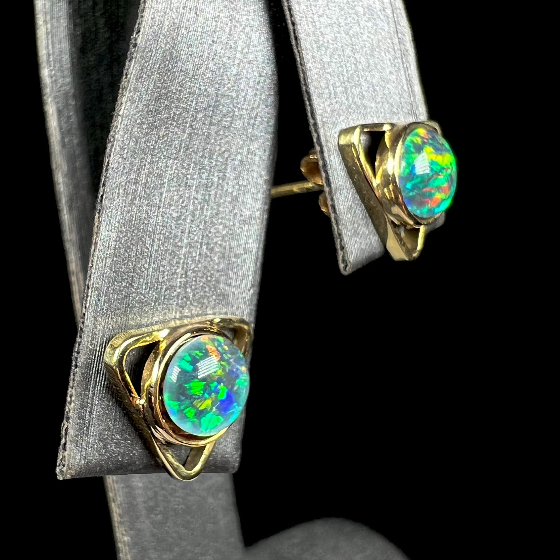 Angled close-up of gold triangle stud earrings set with round black opal triplets.