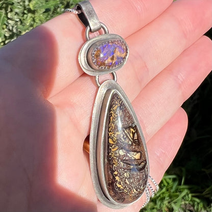 Silver Koroit boulder matrix opal necklace with tribal patterns shown from an angle held in a hand under sunlight.