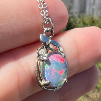 Angled close-up of costume triplet opal necklace in base metal, held in hand under natural light