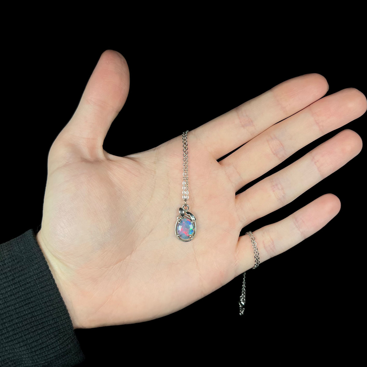 Hand holding triplet opal necklace with pink flashes under cool studio LED light against black background