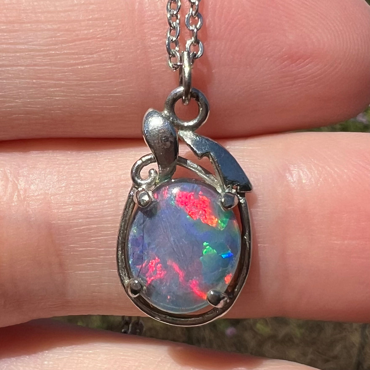 Close-up of costume opal triplet pendant, held in sunlight; the opal has red and green flashes of color