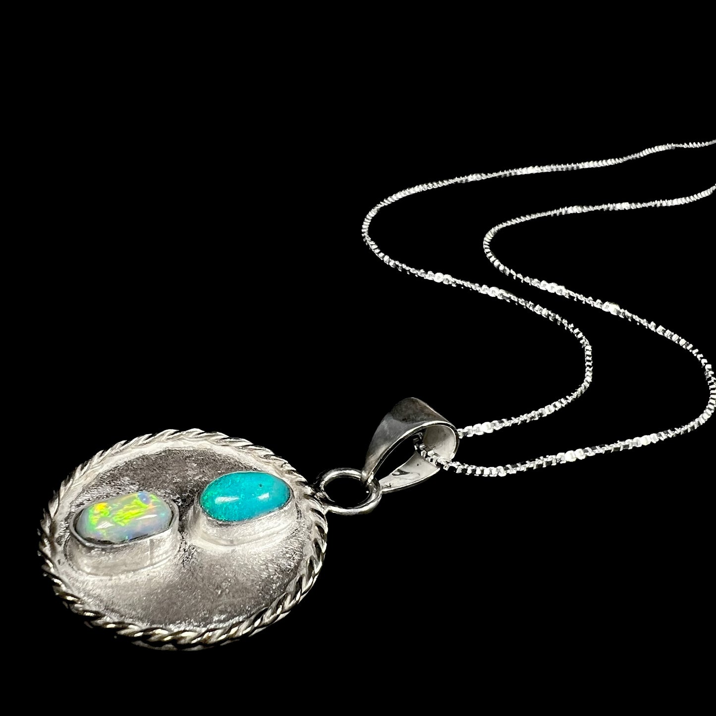Angled view of a sterling silver two-stone Australian semi-crystal opal necklace laying on a black backdrop, its silver chain flowing.