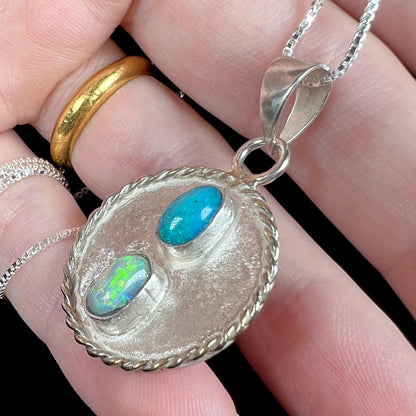 Close-up macro angled view of a two-stone natural opal men's pendant in sterling silver, shown resting on fingers.