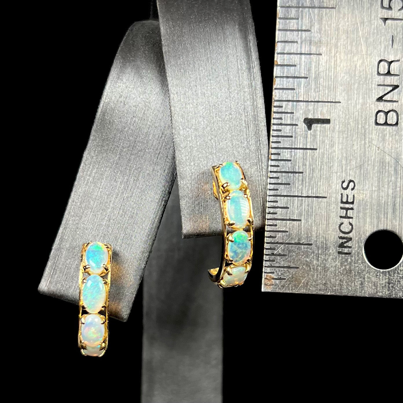 Gold opal semi-hoop earrings that measure two-thirds of an inch long shown on an earring display next to a ruler.