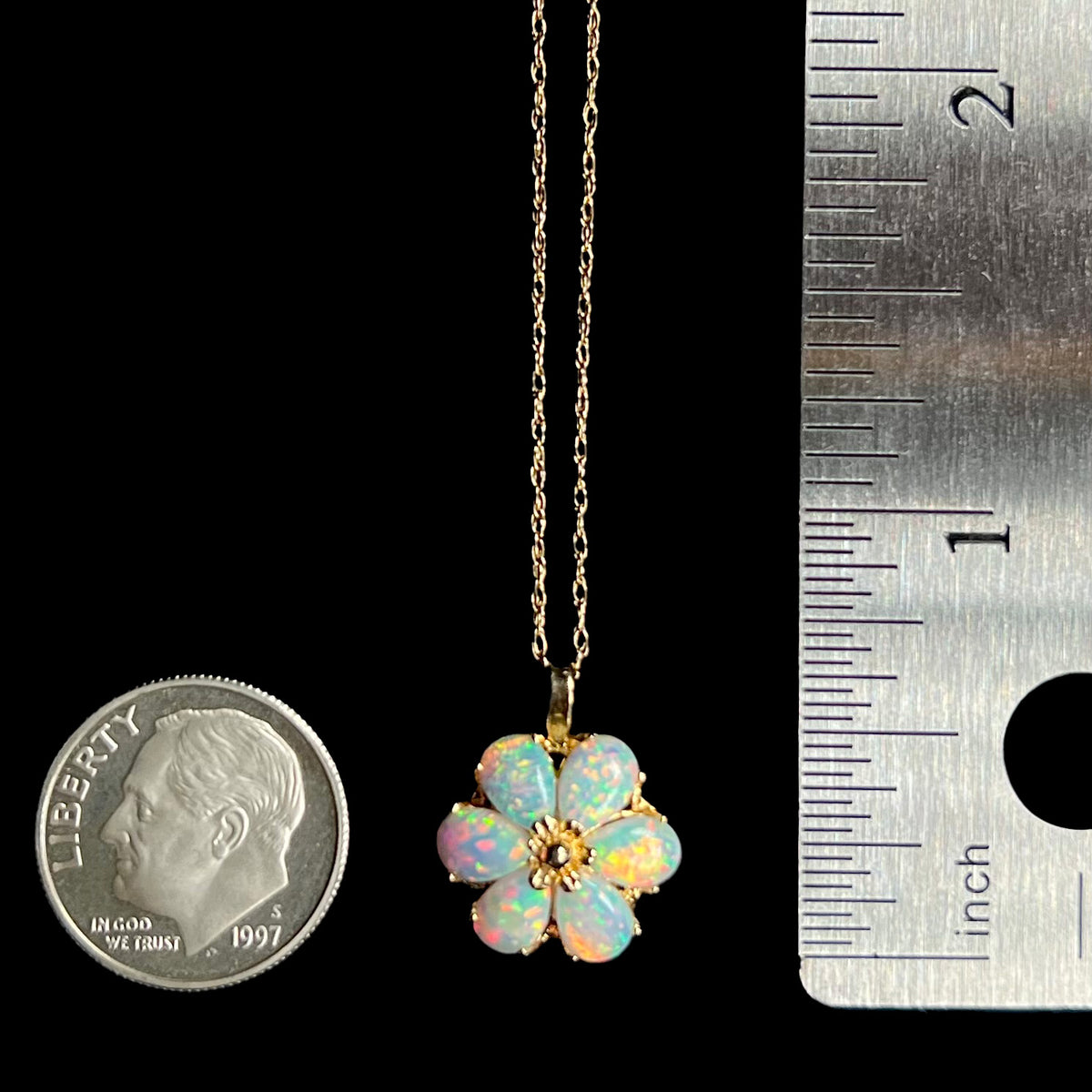Gold lab-created opal flower pendant that measures two-thirds of an inch long, shown between a US dime coin and a ruler