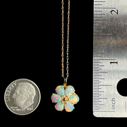Gold lab-created opal flower pendant that measures two-thirds of an inch long, shown between a US dime coin and a ruler
