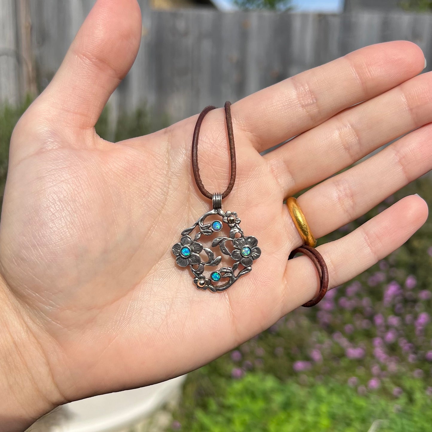 A two-tone sterling silver and 14k gold opal dogwood flower necklace held in a hand, shown in the sunlight.