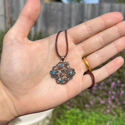A two-tone sterling silver and 14k gold opal dogwood flower necklace held in a hand, shown in the sunlight.