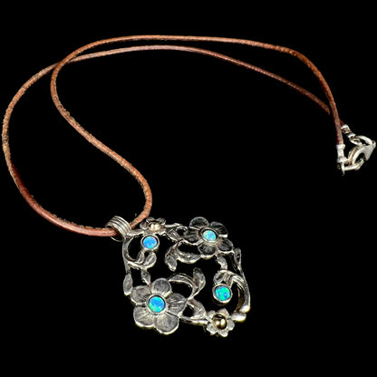A two-tone sterling silver and 14k gold opal dogwood flower necklace shown laying against a black background.