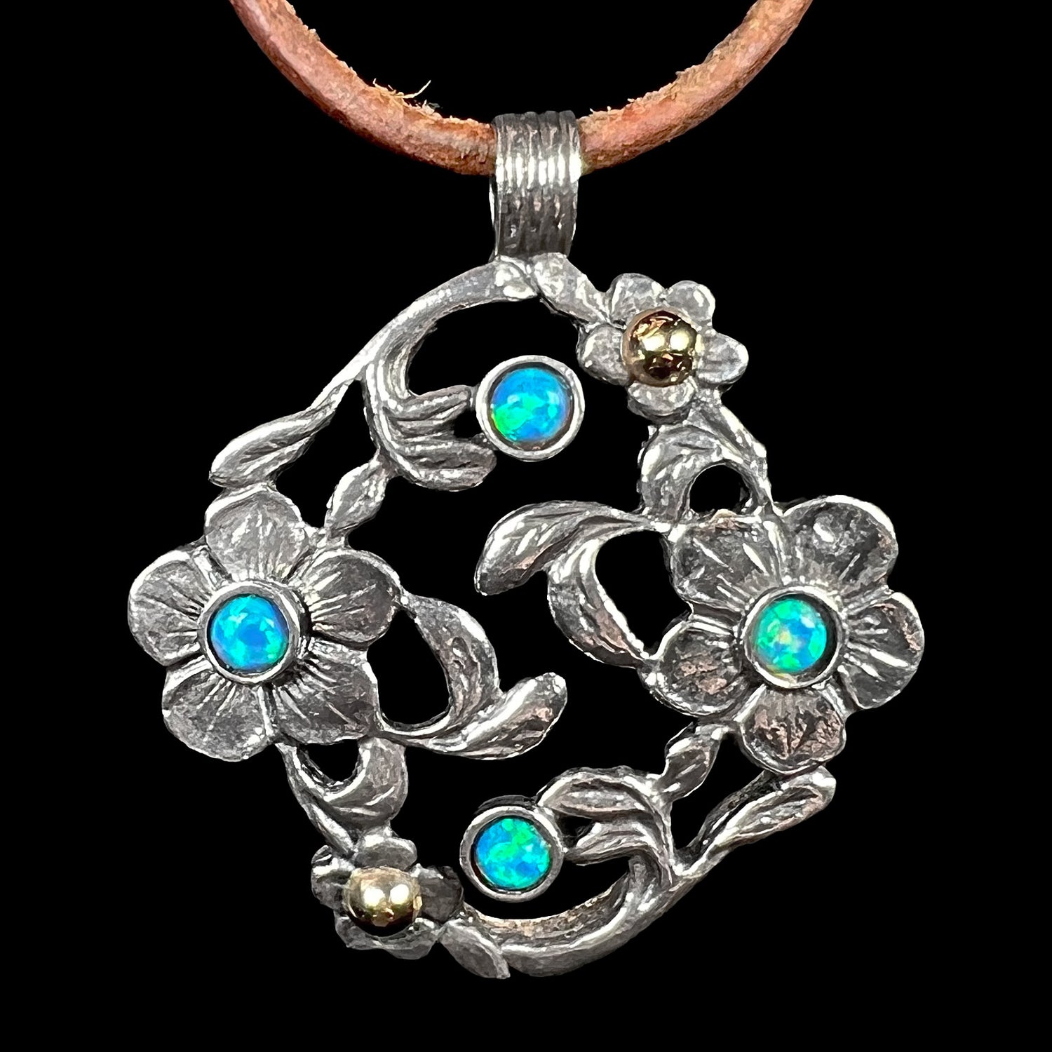 A two-tone sterling silver and 14k gold opal dogwood flower pendant shown on a cord against a black background.