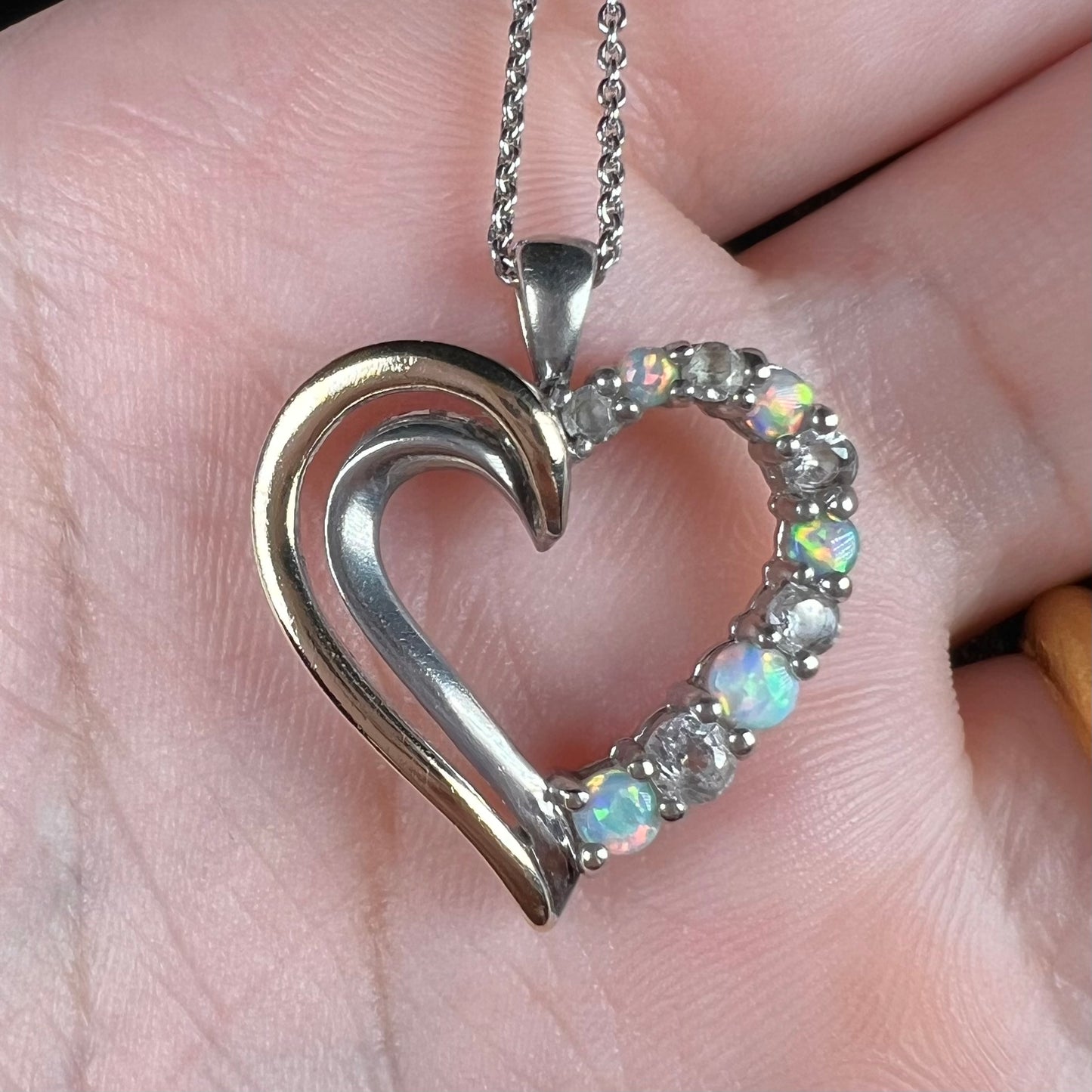 Close-up of a two-tone sterling silver and yellow gold lab-created opal and CZ heart necklace in a hand.
