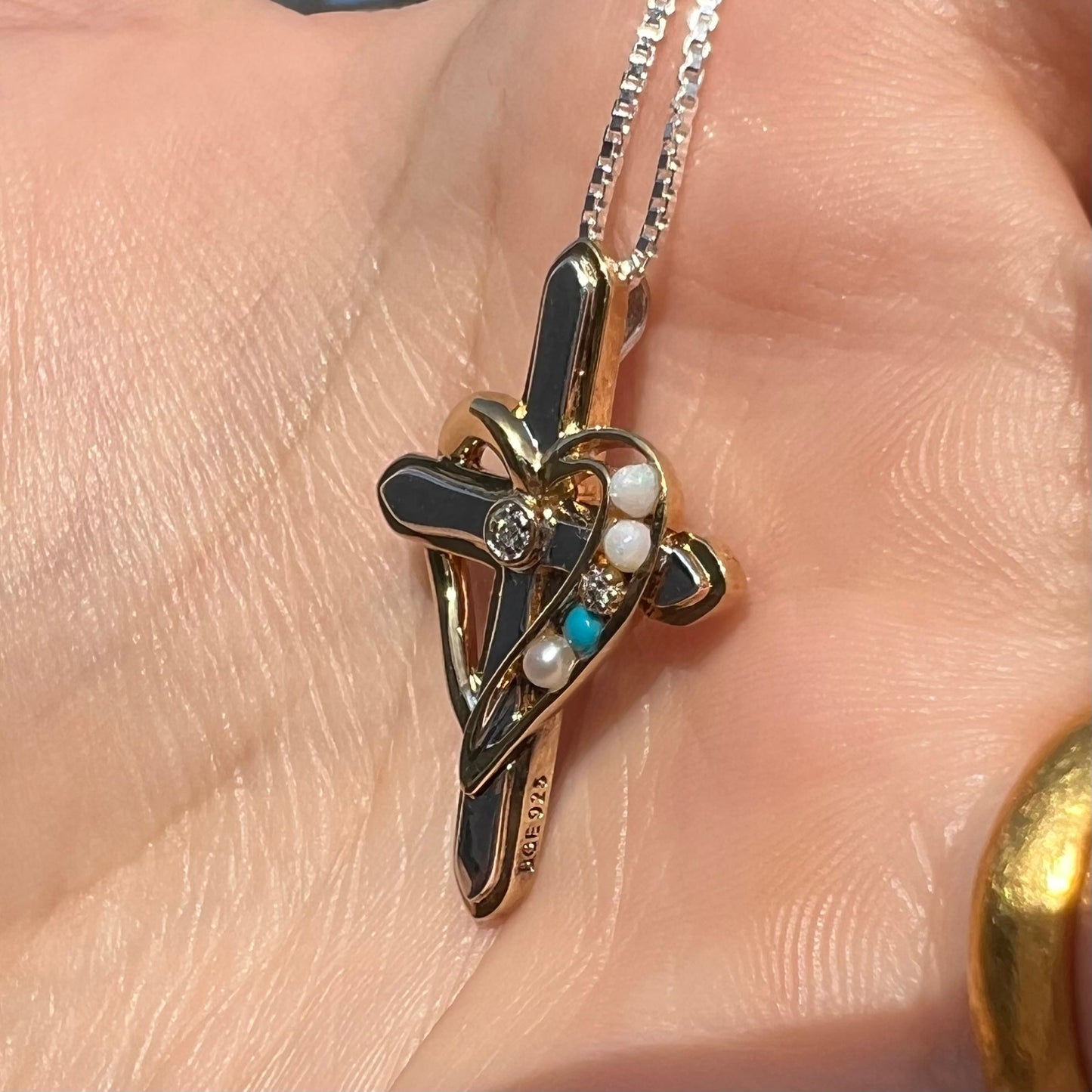 A two-tone sterling silver mother's cross necklace set with diamond, opal, turquoise, and pearl, shown in sunlight.