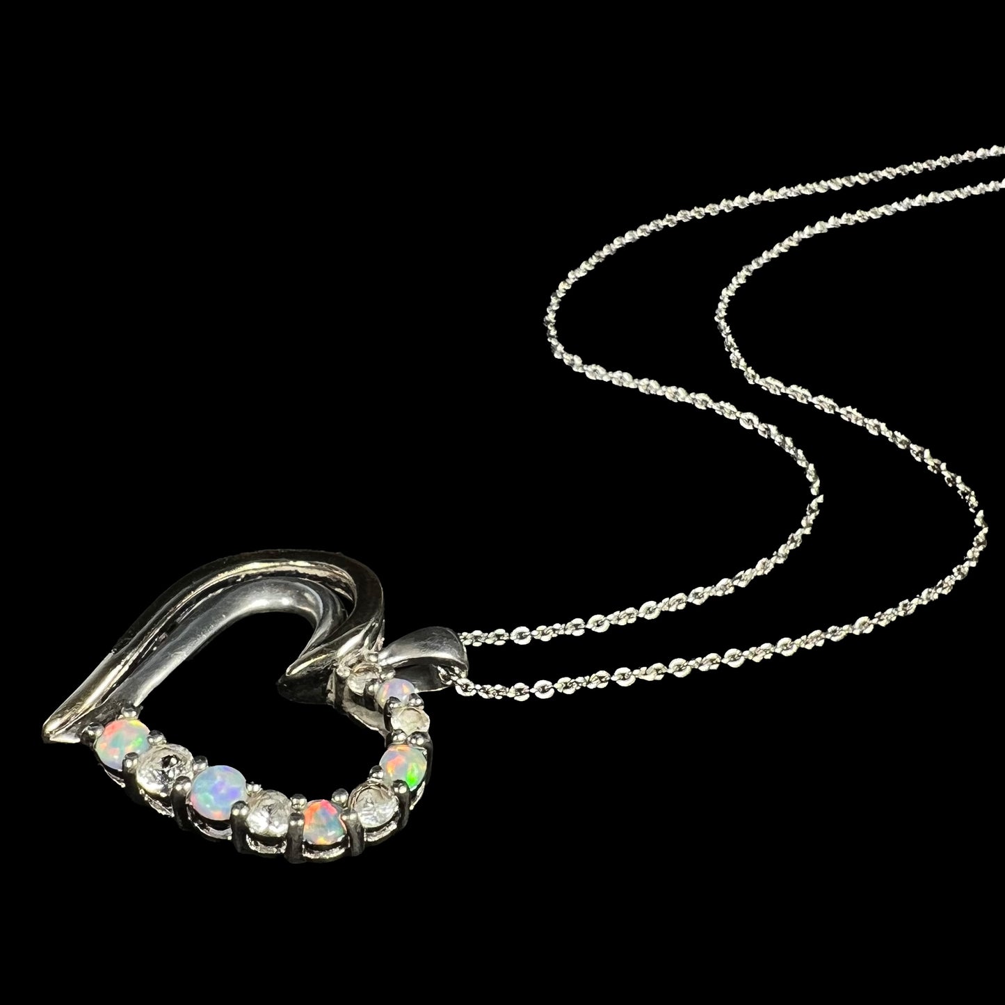 A two-tone sterling silver and yellow gold lab-created opal and CZ heart necklace laying on black background.
