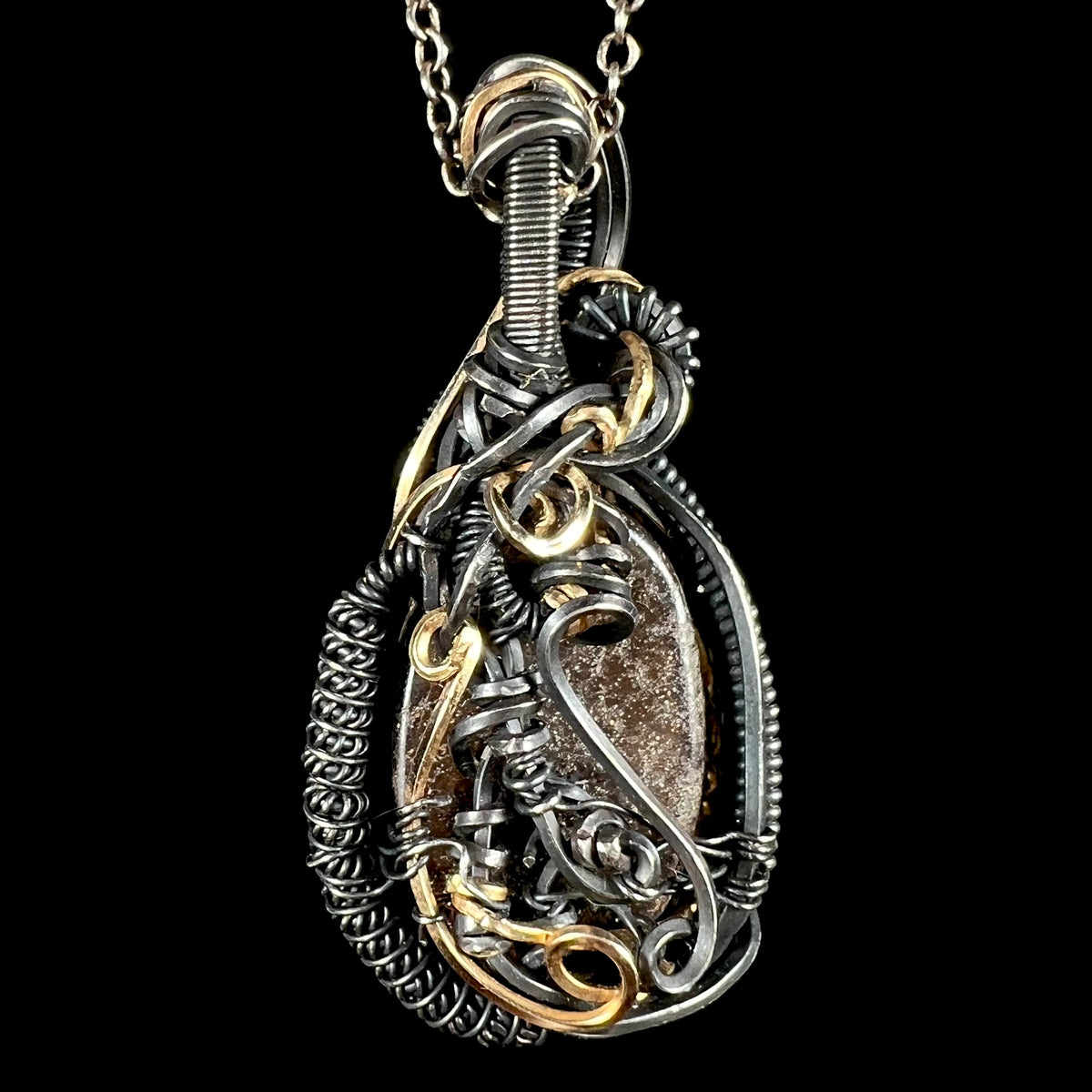 Back side of a two-tone blackened sterling silver and gold-plated wire wrapped pendant set with a boulder opal, its brown ironstone matrix showing.