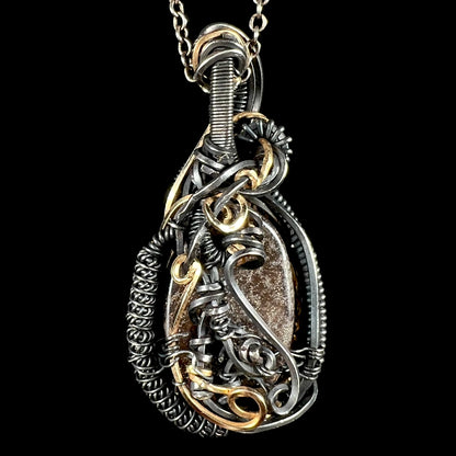 Back side of a two-tone blackened sterling silver and gold-plated wire wrapped pendant set with a boulder opal, its brown ironstone matrix showing.