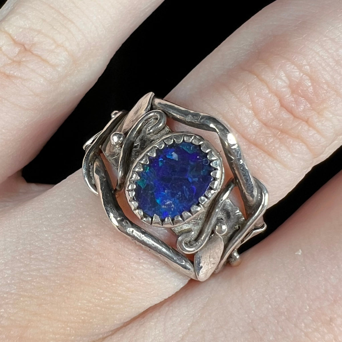 Close-up of sterling silver Australian black opal doublet ring with unique nature-inspired vine and leaf design, worn on finger