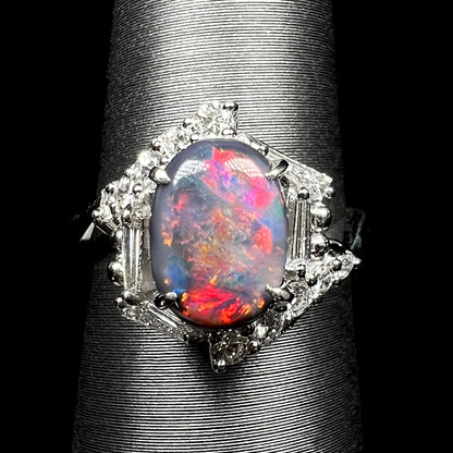 Close-up of unique Australian dark opal engagement ring with geometric halo set with round and tapered baguette cut diamonds, shown on ring display.