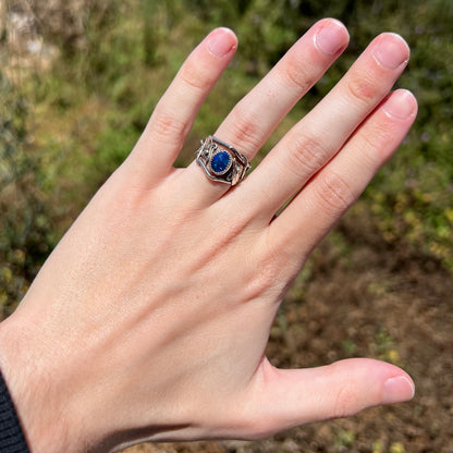 Hand wearing unique women's sterling silver black opal doublet ring with twisting vine and leaf design in sunlight