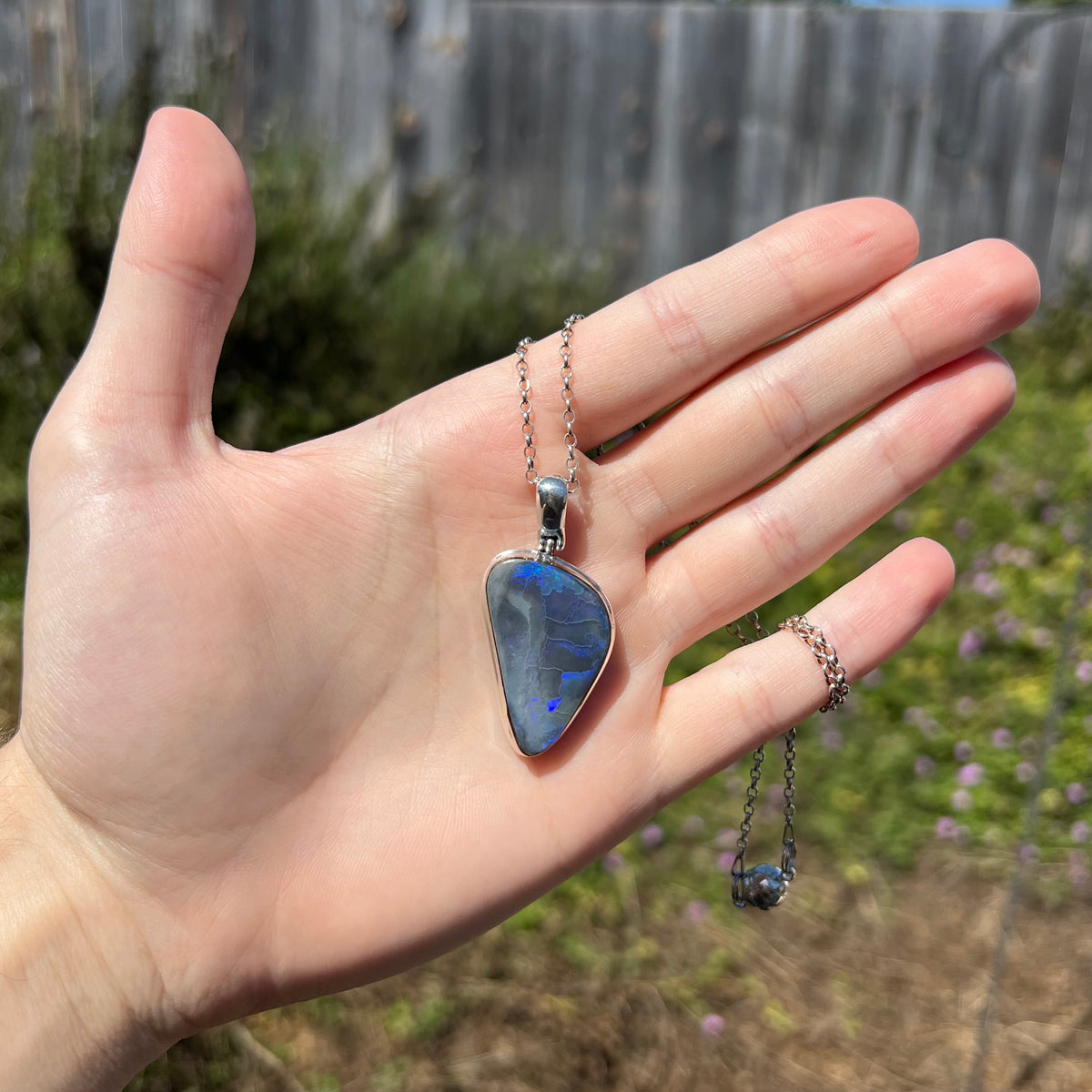 Unisex sterling silver black opal necklace with magnetic clasp, held in hand in sunlight