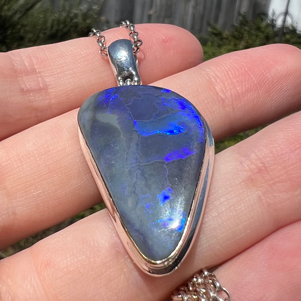Close-up of unisex silver black opal pendant, held in hand under sunlight, viewed from bottom-side-up